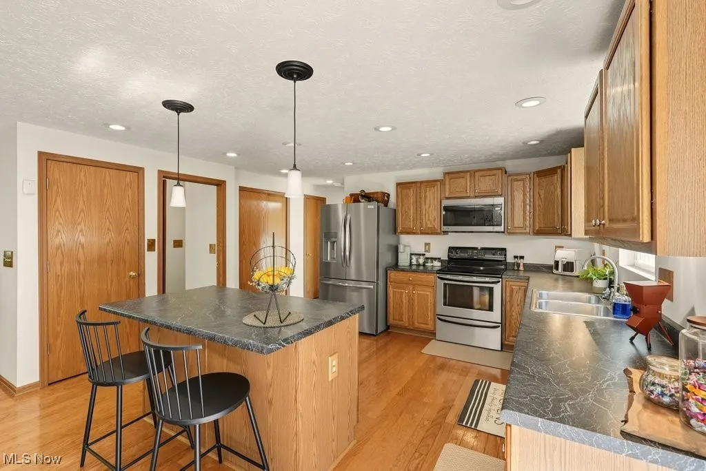 Kitchen with stainless steel appliances, a kitchen bar, light wood-style flooring, hanging light fixtures, and dark countertops