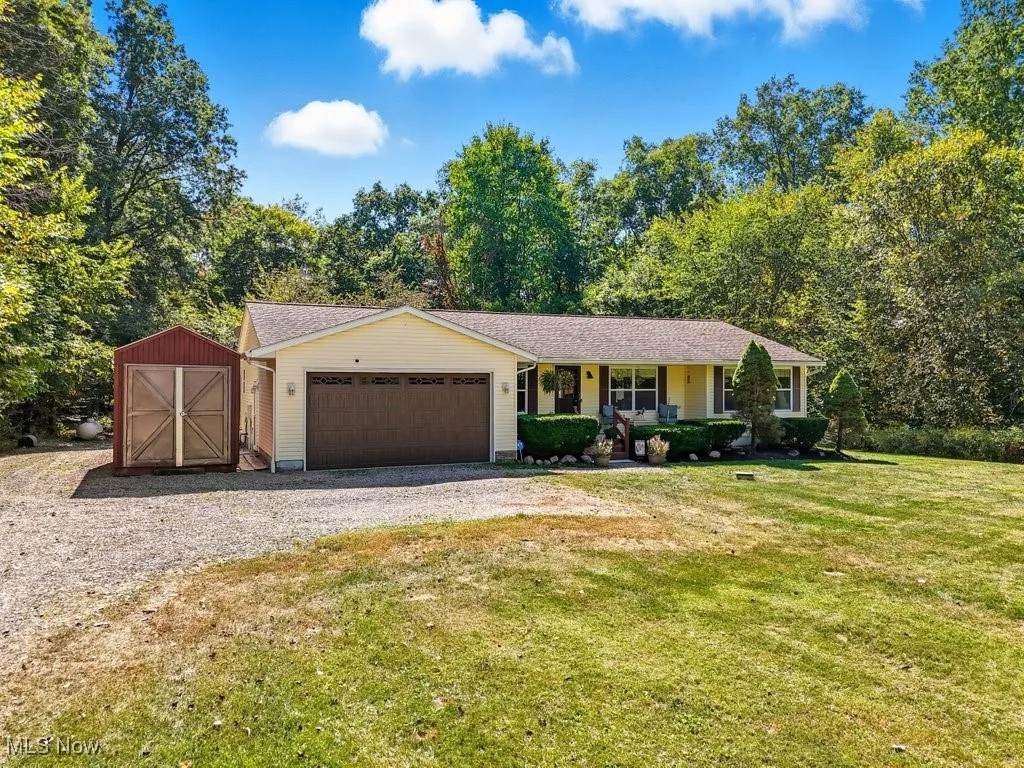 Ranch-style house featuring covered porch, gravel driveway, a front lawn, and a garage