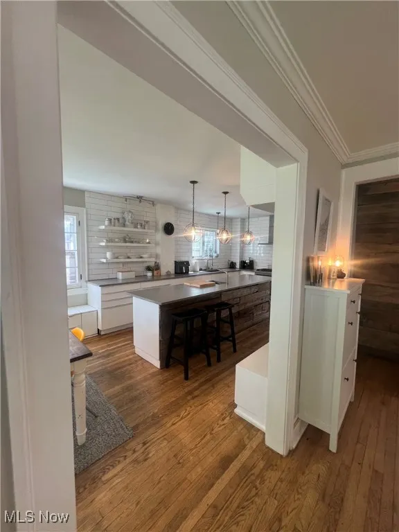Kitchen featuring white cabinetry, decorative light fixtures, dark wood-type flooring, open shelves, and ornamental molding