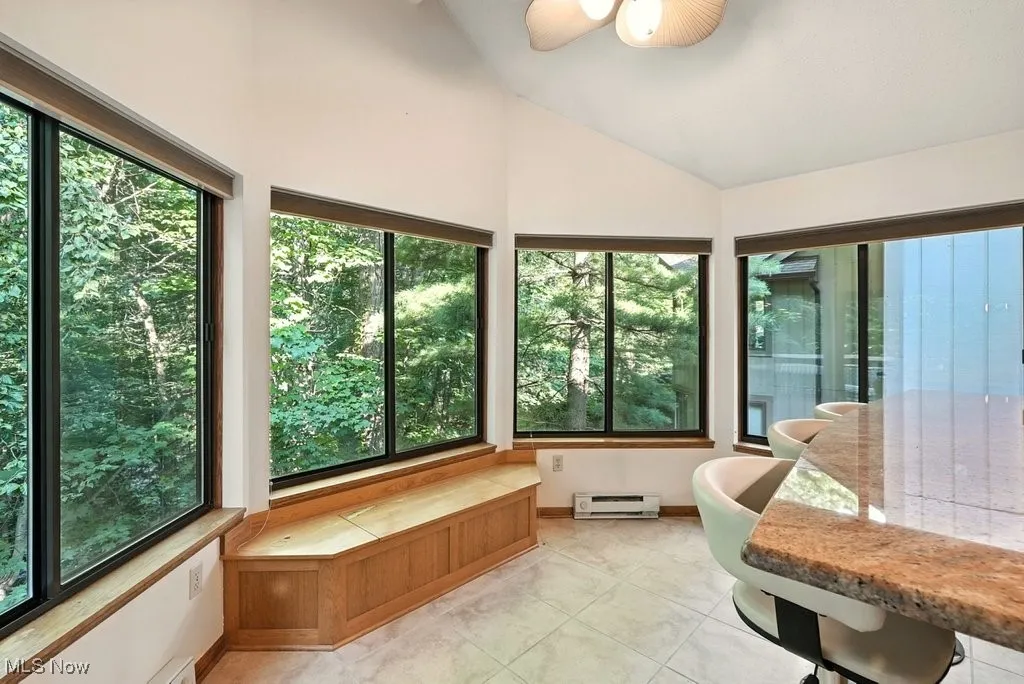 Sunroom with lofted ceiling, a baseboard heating unit, and tile patterned floors