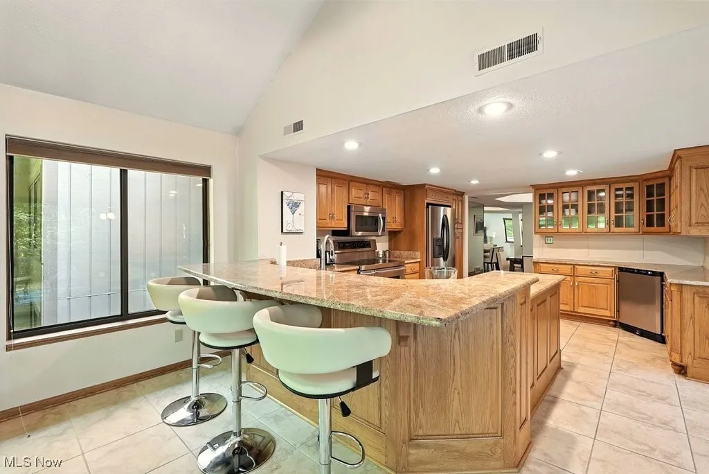 Kitchen with glass insert cabinets, light tile patterned floors, appliances with stainless steel finishes, a peninsula, and recessed lighting