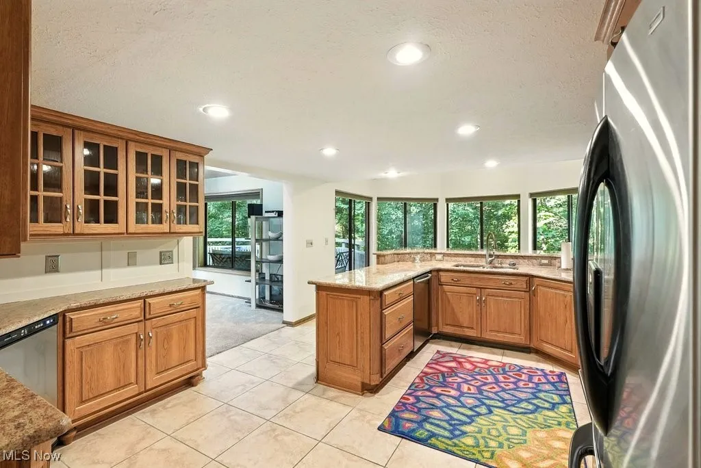 Kitchen with glass insert cabinets, stainless steel appliances, brown cabinets, a peninsula, and light tile patterned floors