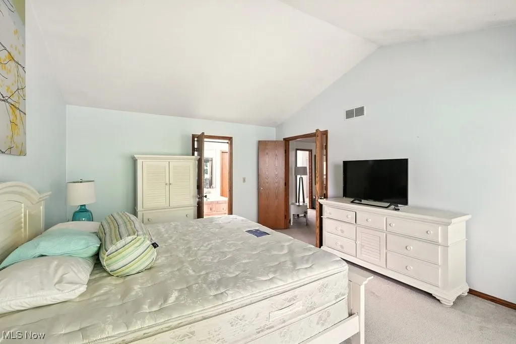 Bedroom with light carpet, lofted ceiling, and connected bathroom