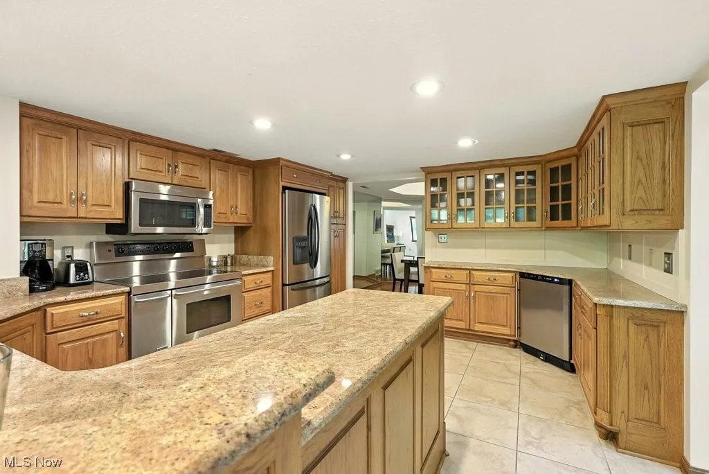 Kitchen featuring appliances with stainless steel finishes, recessed lighting, light tile patterned floors, brown cabinets, and light stone countertops