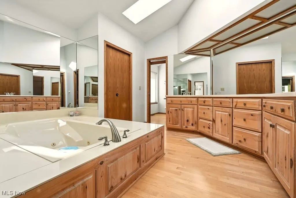 Full bath with a whirlpool tub, a skylight, vanity, light wood-style flooring, and vaulted ceiling