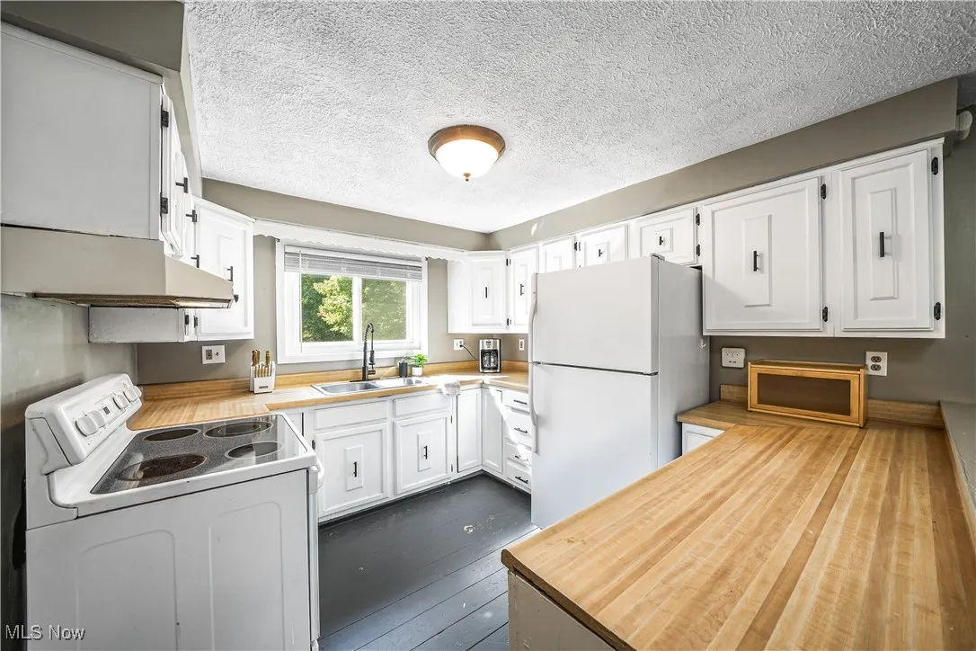Kitchen featuring white appliances, white cabinets, a textured ceiling, dark wood-style floors, and under cabinet range hood