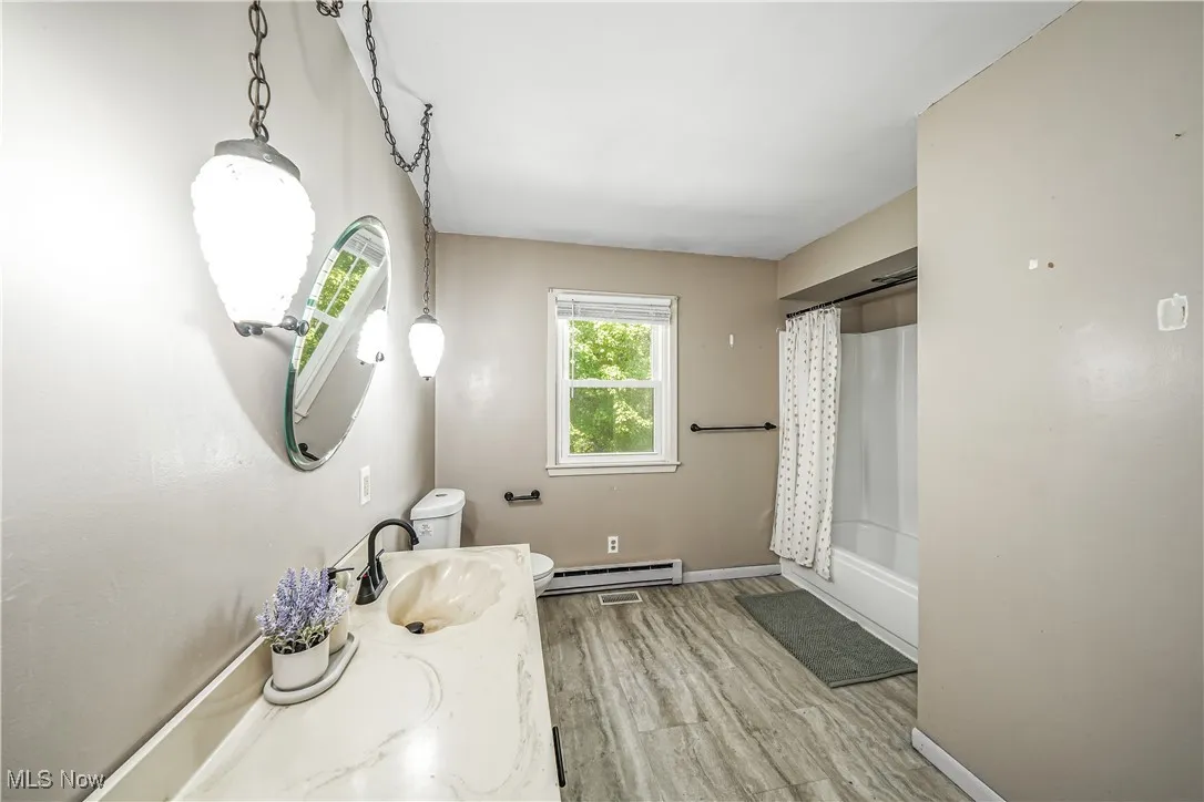 Full bathroom with vanity, shower / bath combo, light wood-type flooring, and baseboard heating