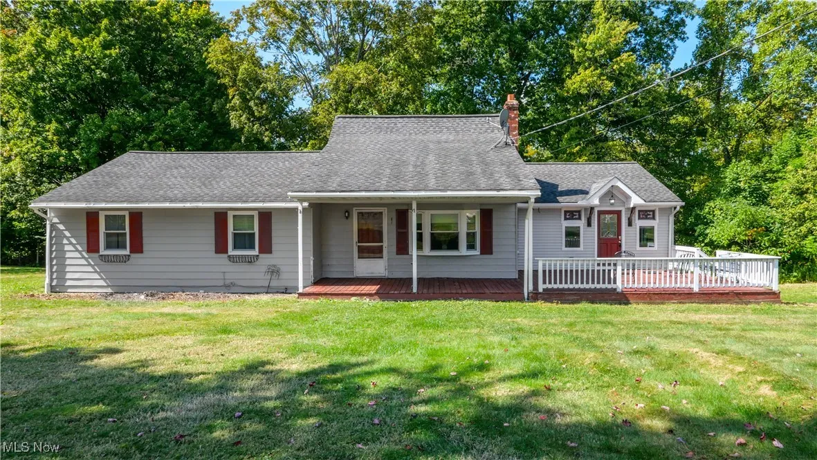 Ranch-style home featuring a front yard, a chimney, a shingled roof, and a deck