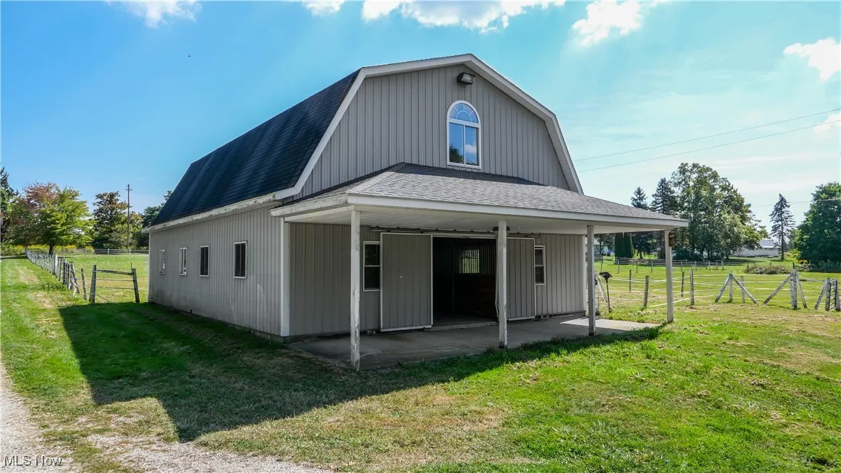 Back of property with a gambrel roof, roof with shingles, and a patio area