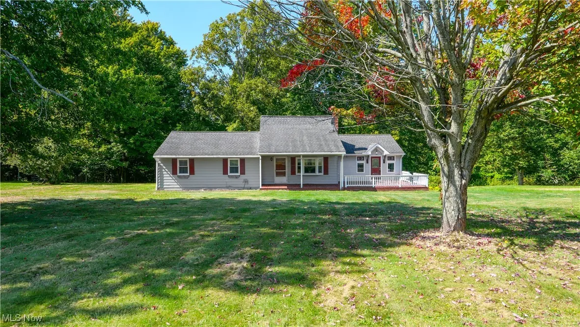 View of front of home featuring a front yard, view of wooded area, and a wooden deck