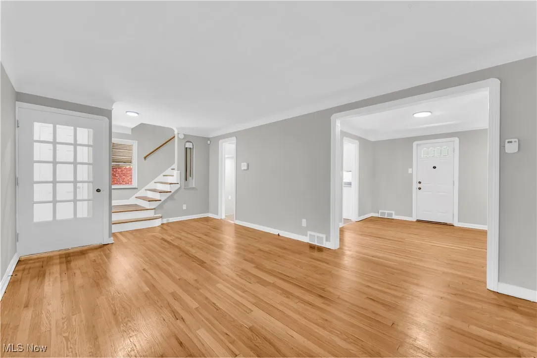 Unfurnished living room with light wood-style flooring, stairs, and ornamental molding