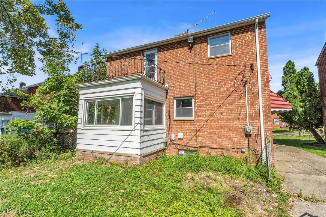 Rear view of property with a sunroom, a balcony, brick siding, and a lawn