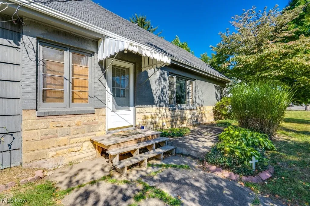 Doorway to property with roof with shingles, stone siding, and brick siding