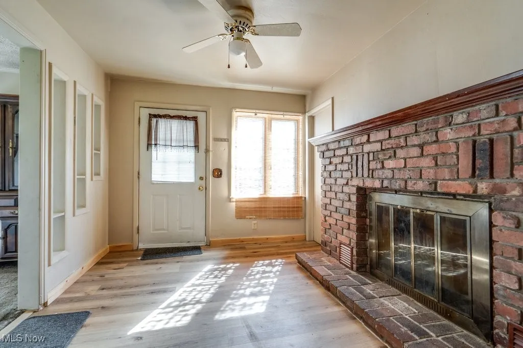 Doorway with a fireplace, wood finished floors, and ceiling fan
