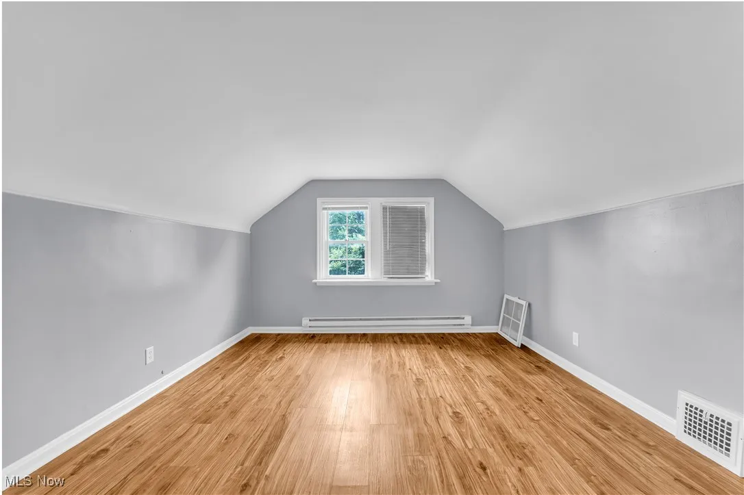 Additional living space with vaulted ceiling, light wood finished floors, and baseboard heating