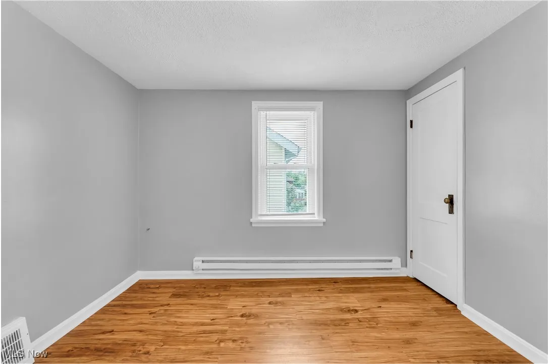 Empty room with a textured ceiling, light wood-style flooring, and a baseboard radiator