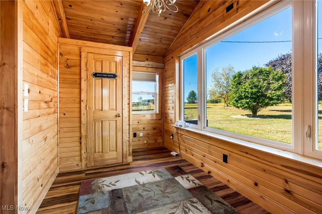 Doorway to outside with wood walls, wood finished floors, wooden ceiling, and a chandelier