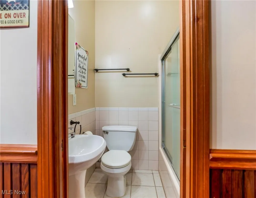 Bathroom with light tile patterned floors, wainscoting, tile walls, and combined bath / shower with glass door