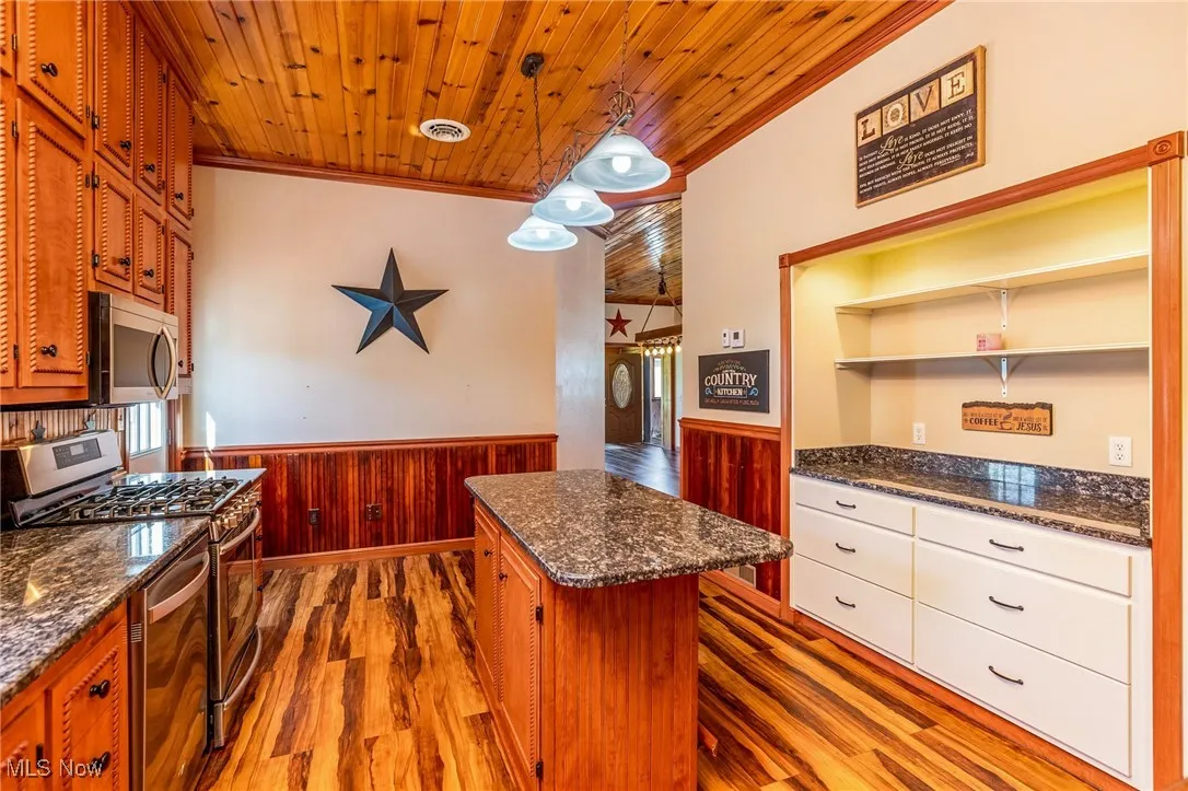Kitchen featuring a wainscoted wall, wooden walls, hanging light fixtures, dark wood finished floors, and ornamental molding