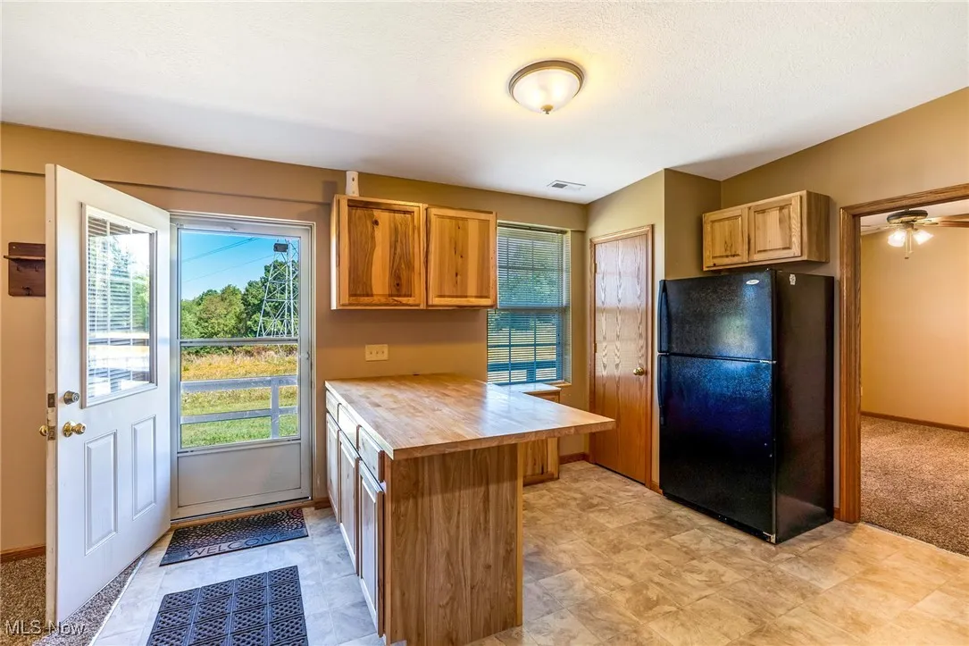 Kitchen featuring a peninsula, freestanding refrigerator, brown cabinetry, and wood counters