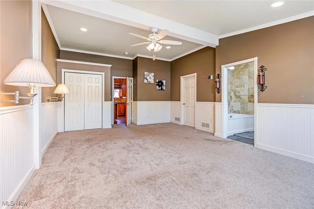 Unfurnished bedroom with ensuite bath, beam ceiling, a closet, light carpet, and a ceiling fan