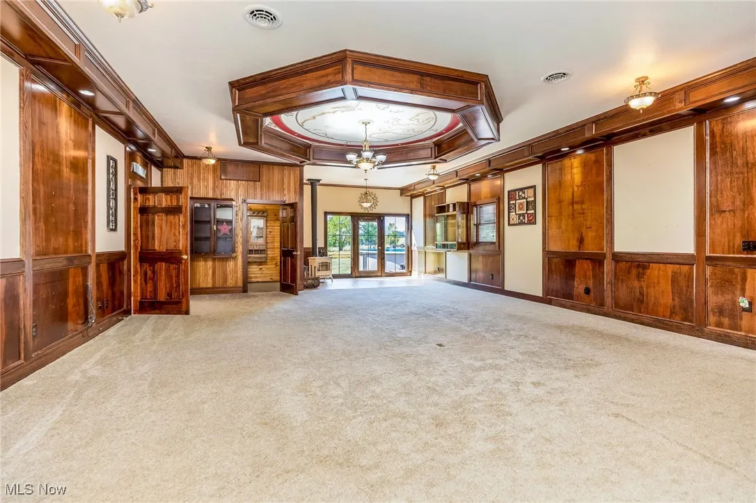 Empty room with wood walls, a raised ceiling, carpet floors, and ornamental molding