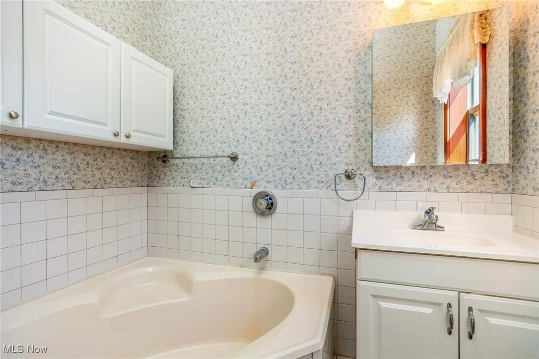 Full bathroom with vanity, a bath, tile walls, wallpapered walls, and wainscoting