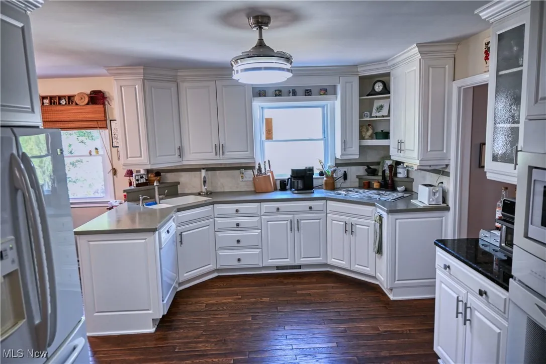 Kitchen with stainless steel fridge, white cabinetry, dark wood-style flooring, a peninsula, and white dishwasher
