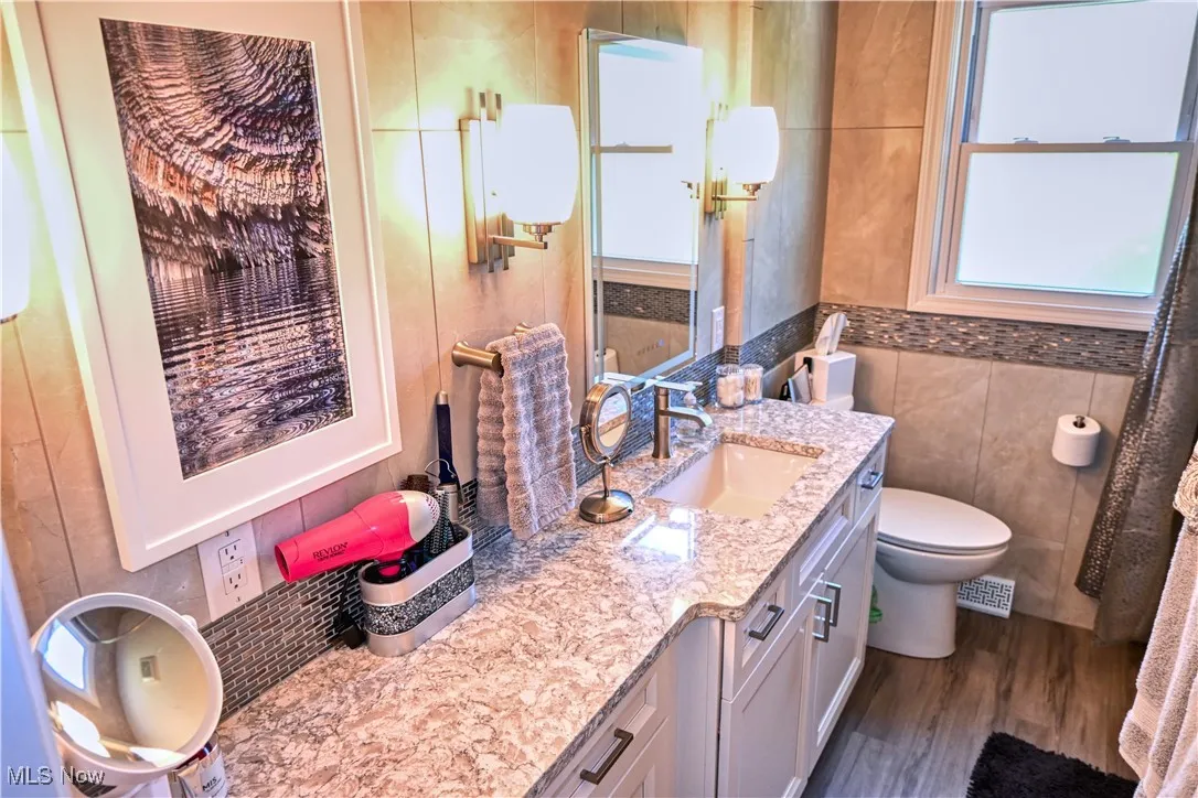 Bathroom with vanity, dark wood finished floors, and tile walls