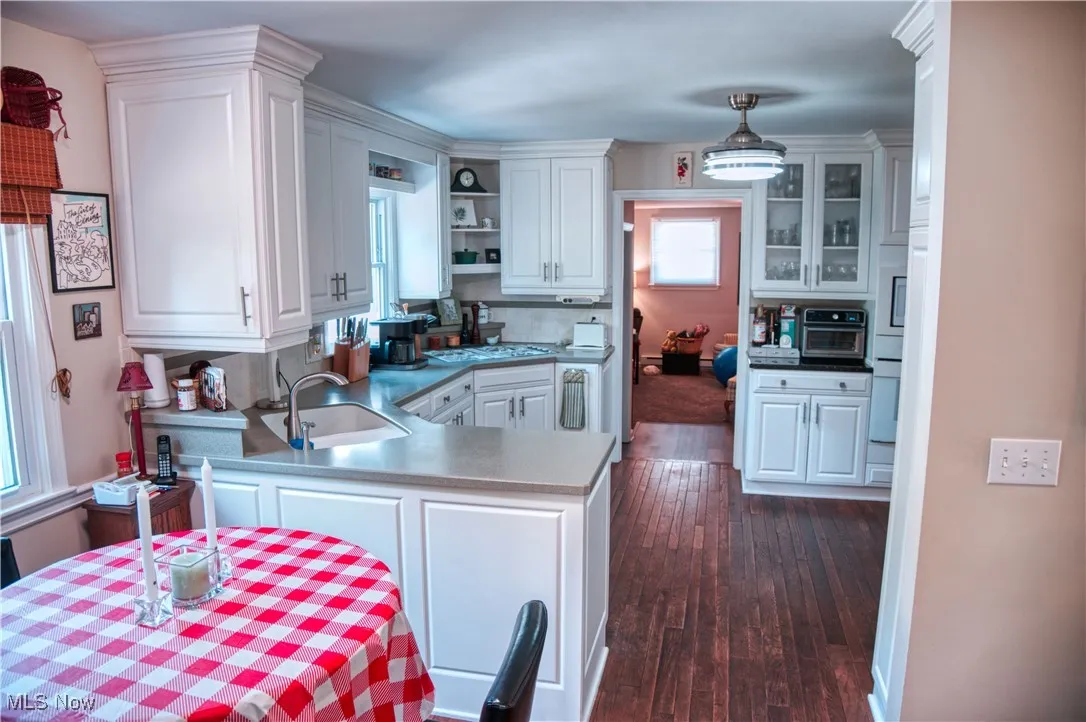Kitchen with white cabinets, a peninsula, dark wood-style floors, open shelves, and hanging light fixtures
