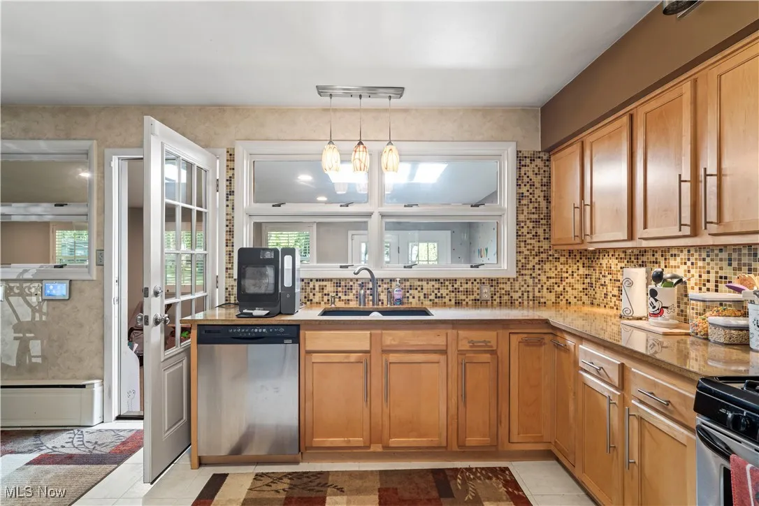 Kitchen featuring dishwasher, backsplash, decorative light fixtures, and brown cabinets