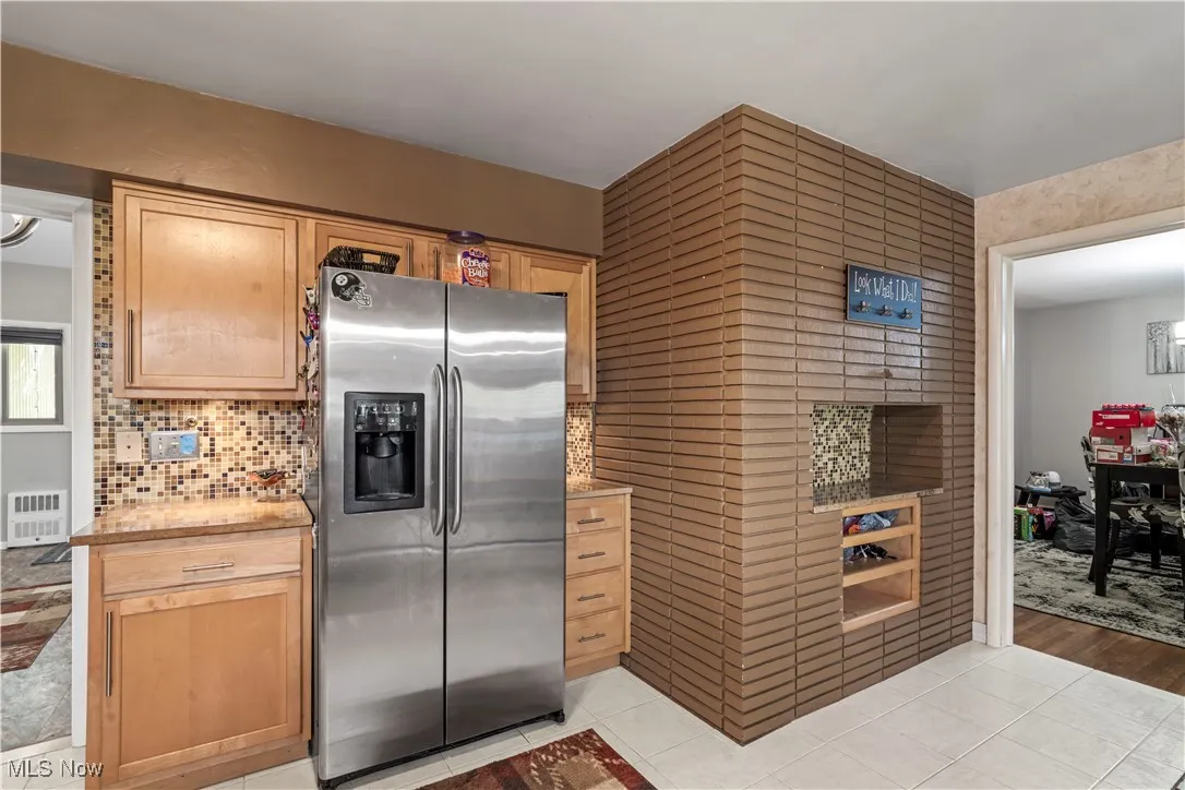 Kitchen featuring stainless steel fridge, light tile patterned flooring, radiator heating unit, and backsplash