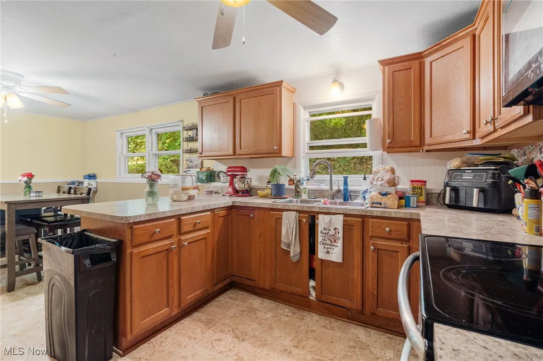 Kitchen featuring range with electric cooktop, a ceiling fan, brown cabinets, and stainless steel microwave