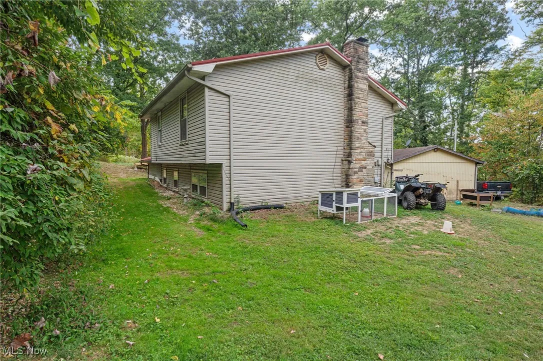 View of property exterior featuring a chimney, a yard, and view of wooded area