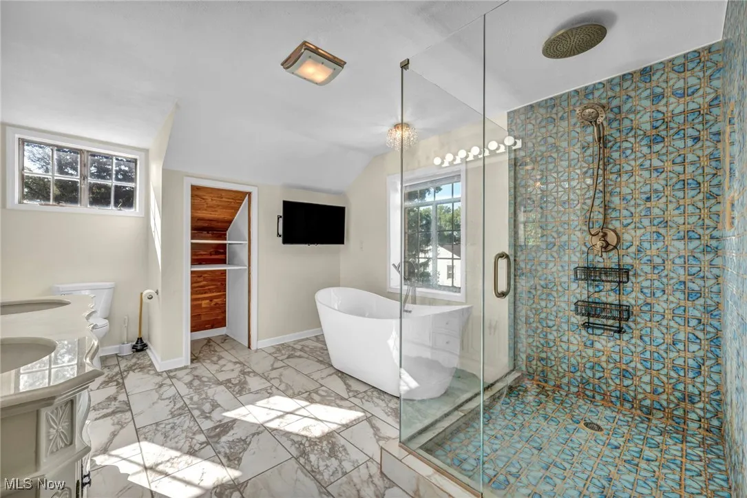 Full bathroom with a soaking tub, a shower stall, vaulted ceiling, light marble finish flooring, and double vanity