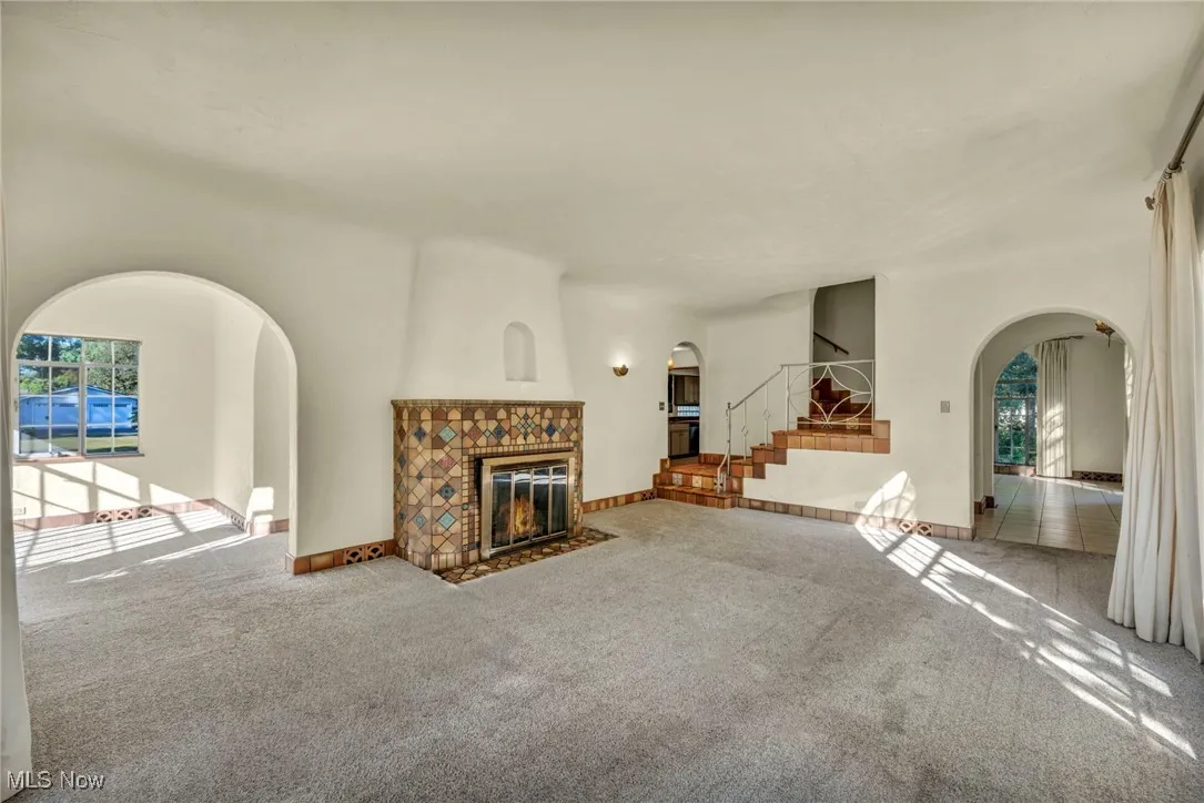 Unfurnished living room with arched walkways, plenty of natural light, a tile fireplace, and carpet