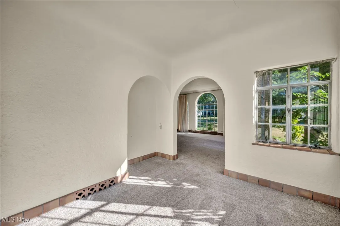 Empty room with a textured wall, arched walkways, and carpet
