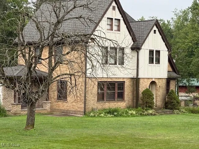Tudor home featuring a front lawn, board and batten siding, brick siding, and a shingled roof