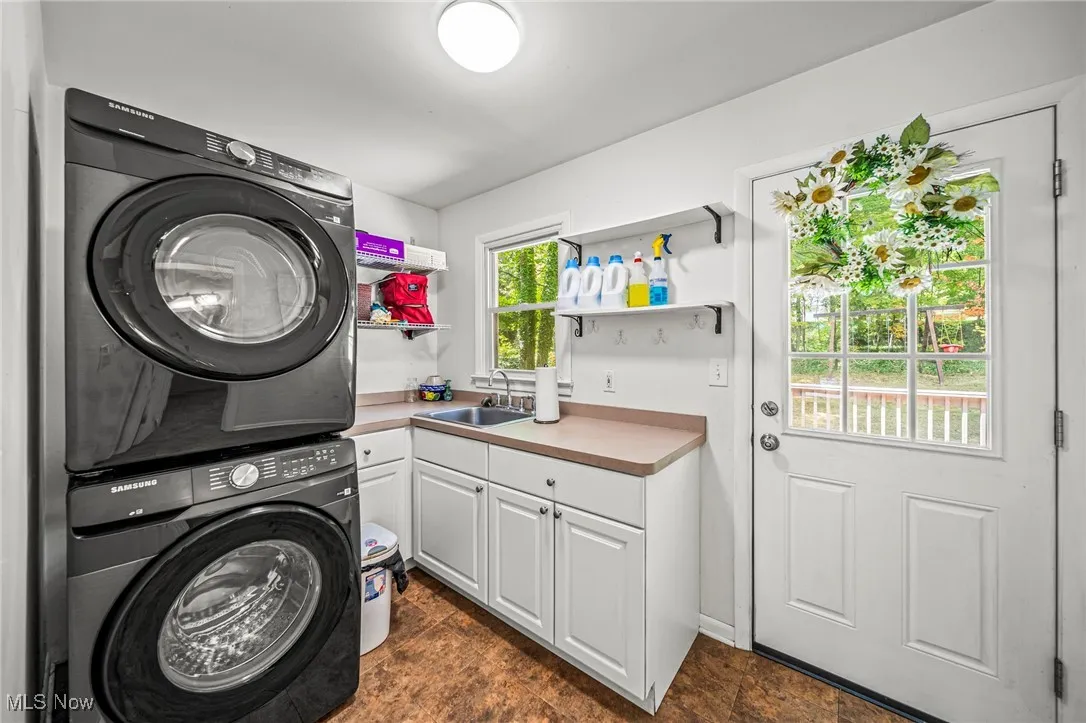 Laundry room with stacked washer and clothes dryer, cabinet space, and dark stone finish flooring