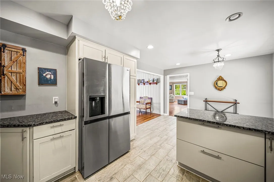 Kitchen with dark stone countertops, decorative light fixtures, stainless steel fridge, a chandelier, and light wood-style floors