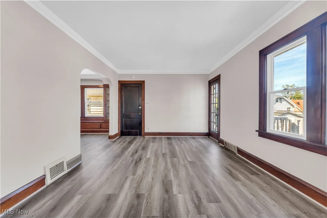 Unfurnished room featuring crown molding, wood finished floors, and arched walkways