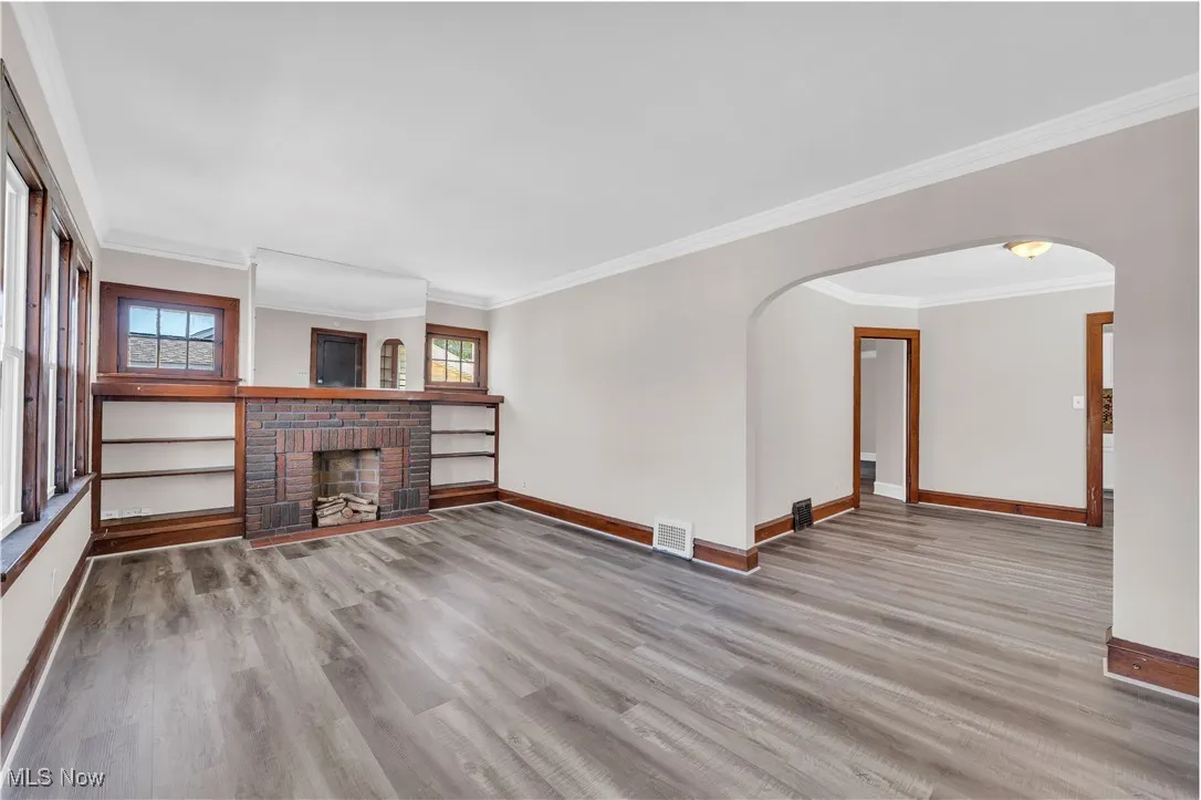 Unfurnished living room featuring crown molding, light wood-style floors, a fireplace, and arched walkways
