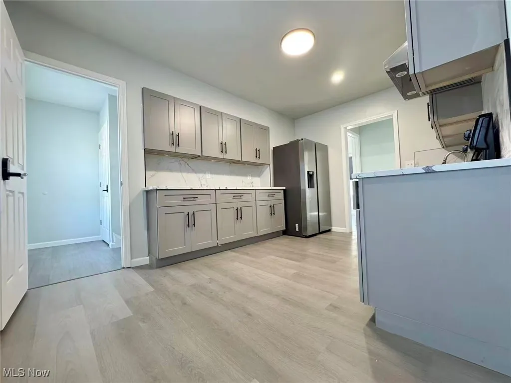 Kitchen with gray cabinetry, stainless steel fridge with ice dispenser, and light wood finished floors