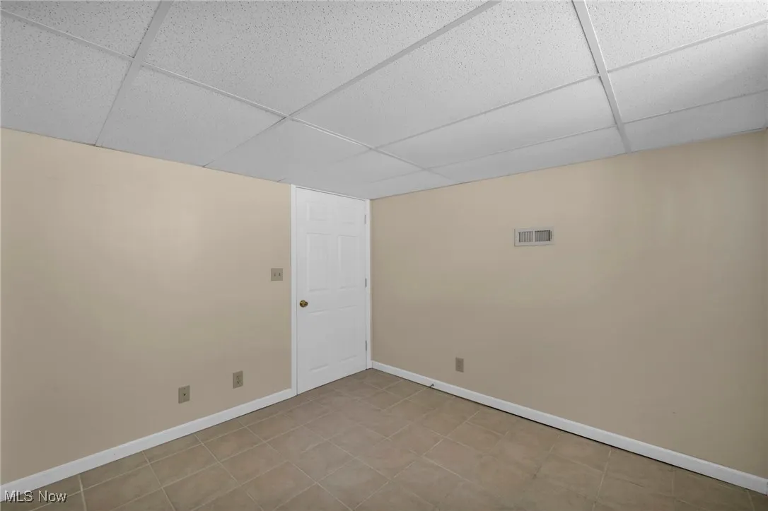 Empty room with a drop ceiling and light tile patterned floors