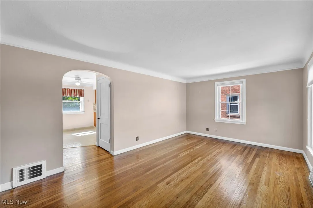 Empty room featuring arched walkways, hardwood / wood-style flooring, crown molding, and a ceiling fan