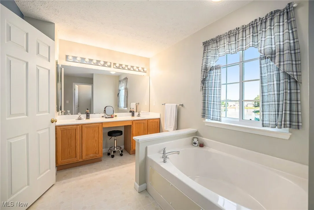 Bathroom featuring double vanity, a textured ceiling, plenty of natural light, and a garden tub