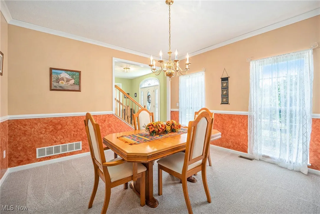 Carpeted dining space featuring crown molding, a chandelier, a wainscoted wall, and stairway