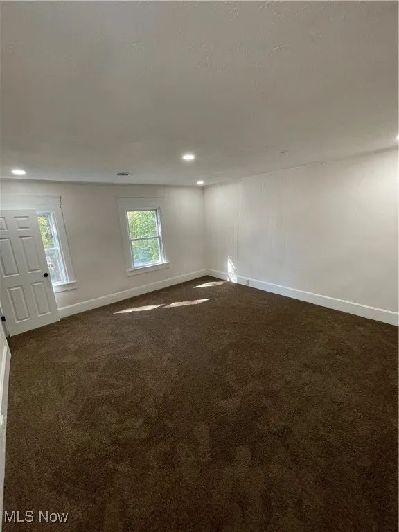 Unfurnished room with dark colored carpet, a textured ceiling, and recessed lighting