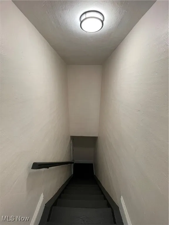 Stairway with a textured ceiling and a textured wall