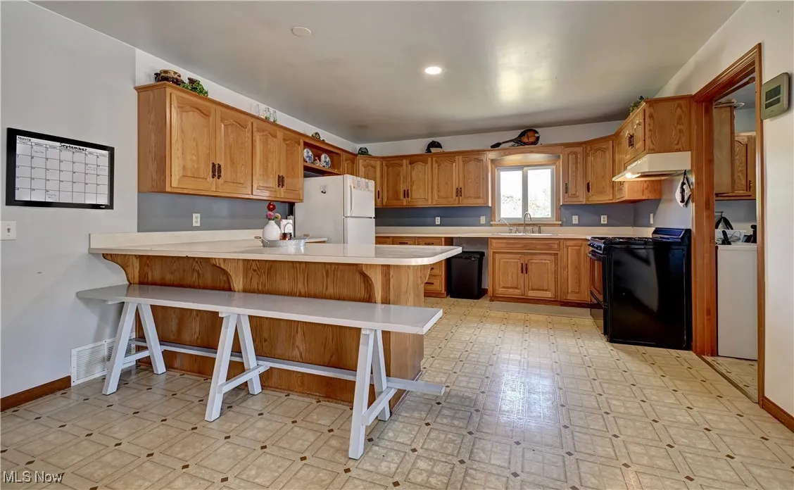 Kitchen with light flooring, light countertops, brown cabinetry, a breakfast bar, and black appliances